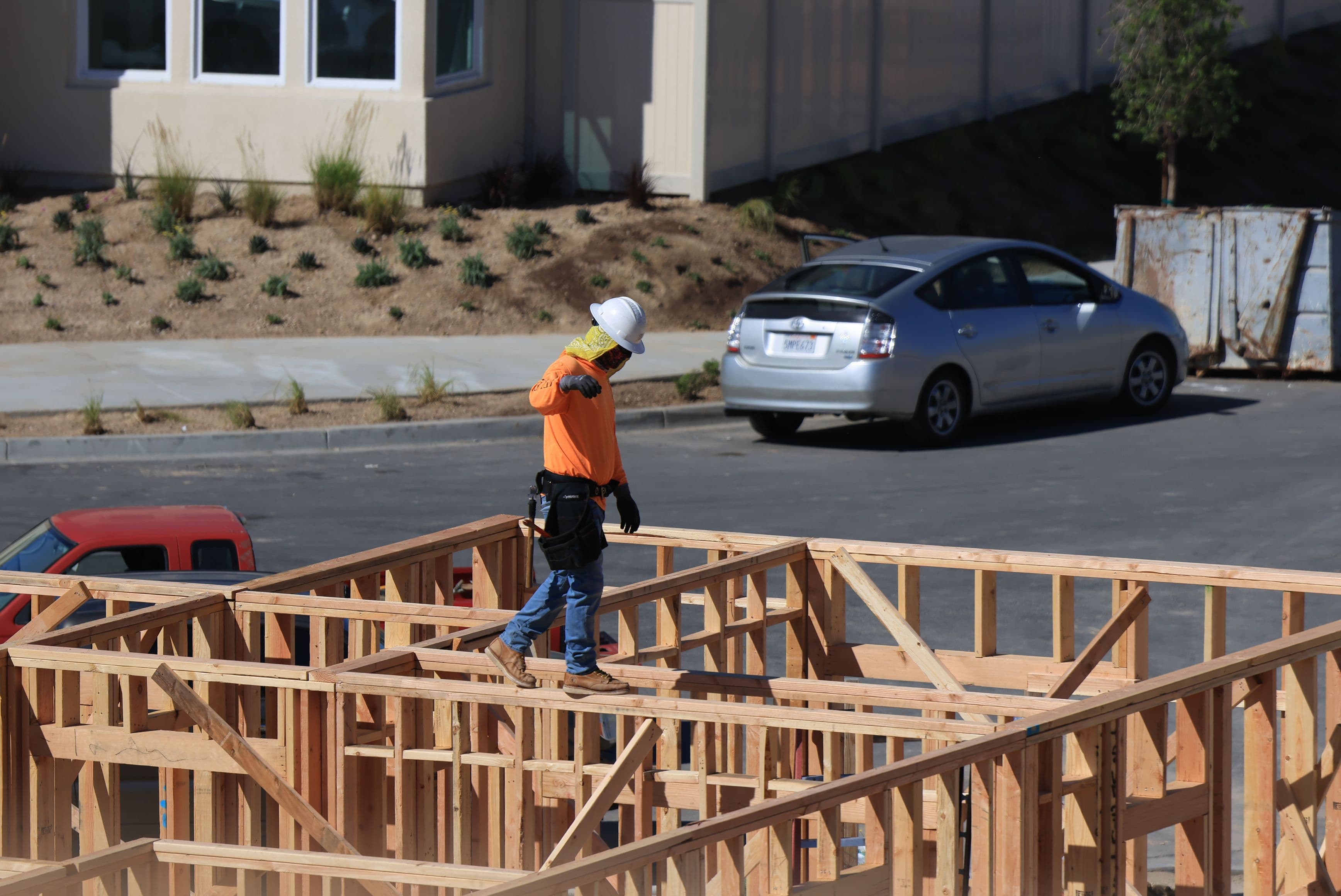 Framer walking a wooden house frame on a suburban street.